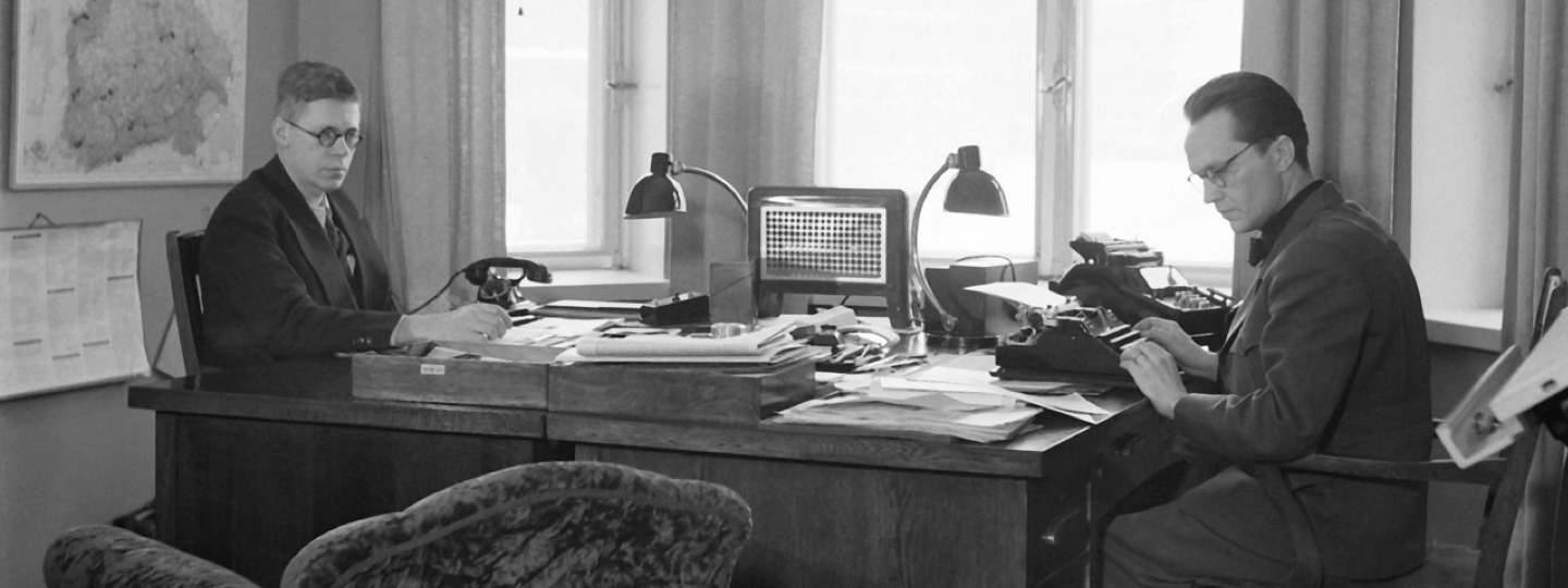 A very old photo of two people working at desks