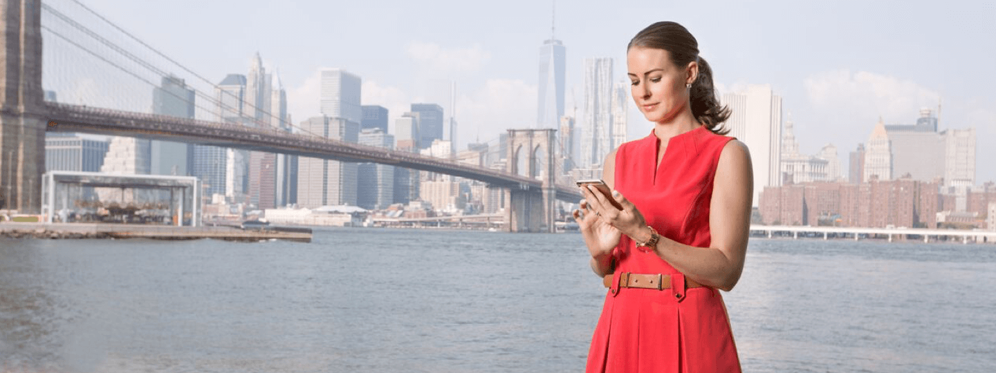 A female in a red dress looking at her phone in front of the New York City skyline