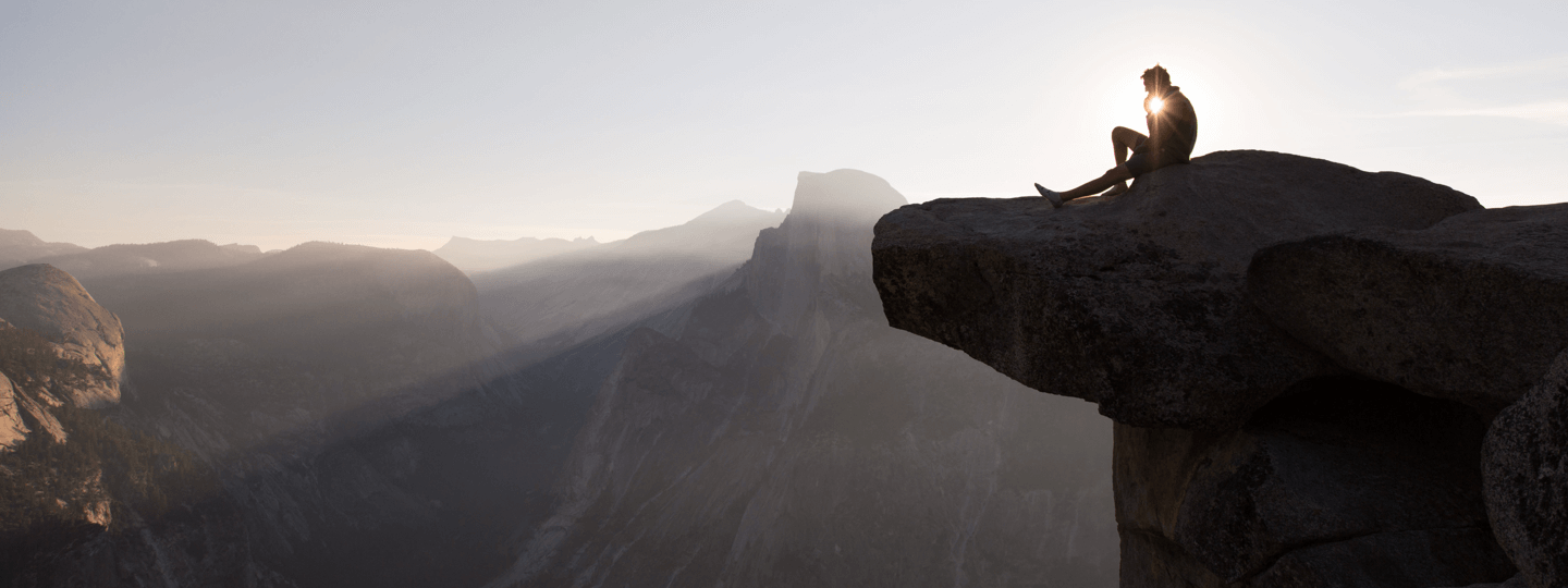 A backlit person sitting on the edge of a cliff in Yosemite National Park