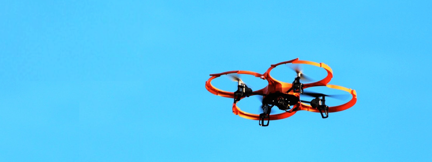 A black and orange drone flies against a blue sky