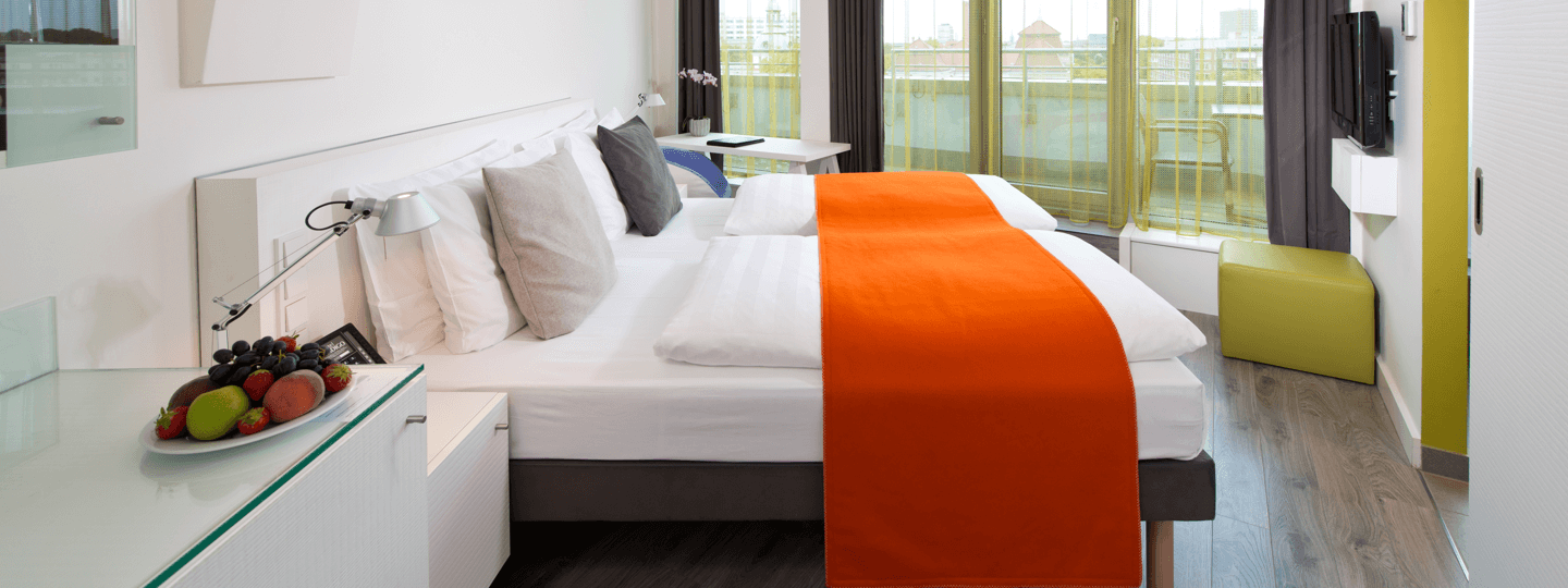 A large bed with an orange throw in a small room