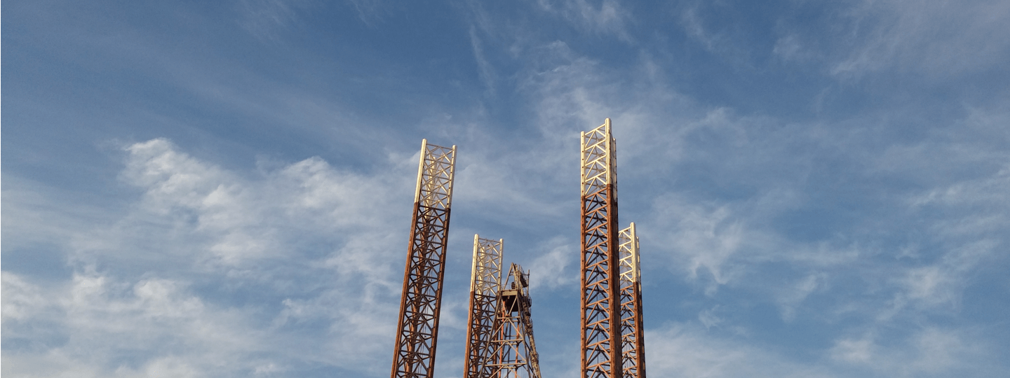 Four oil rig scaffolding pillars against a partly cloudy blue sky