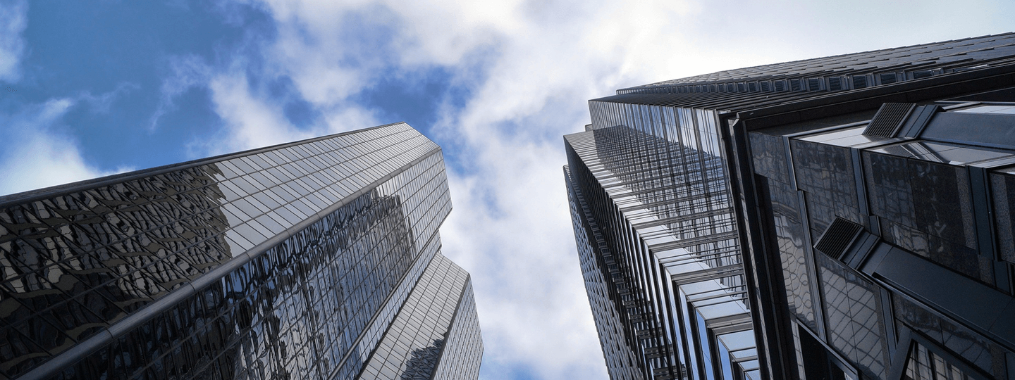 Looking up between two tall office buildings on a partly cloudy day