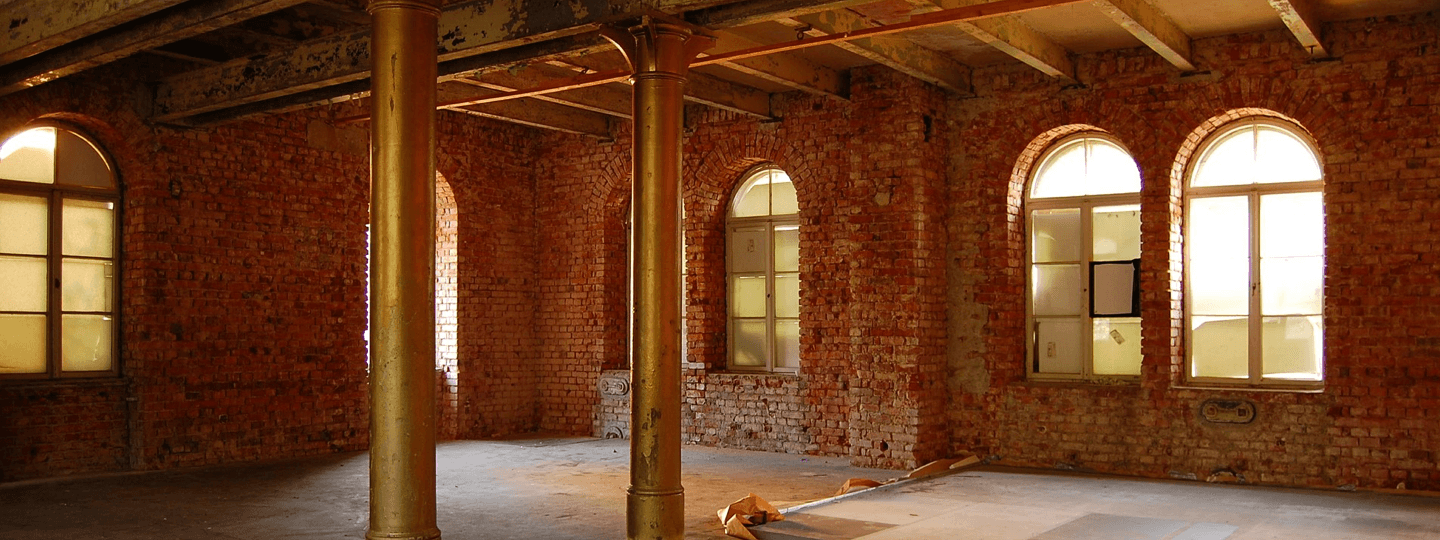 Two large brass support columns within an old, empty brick building