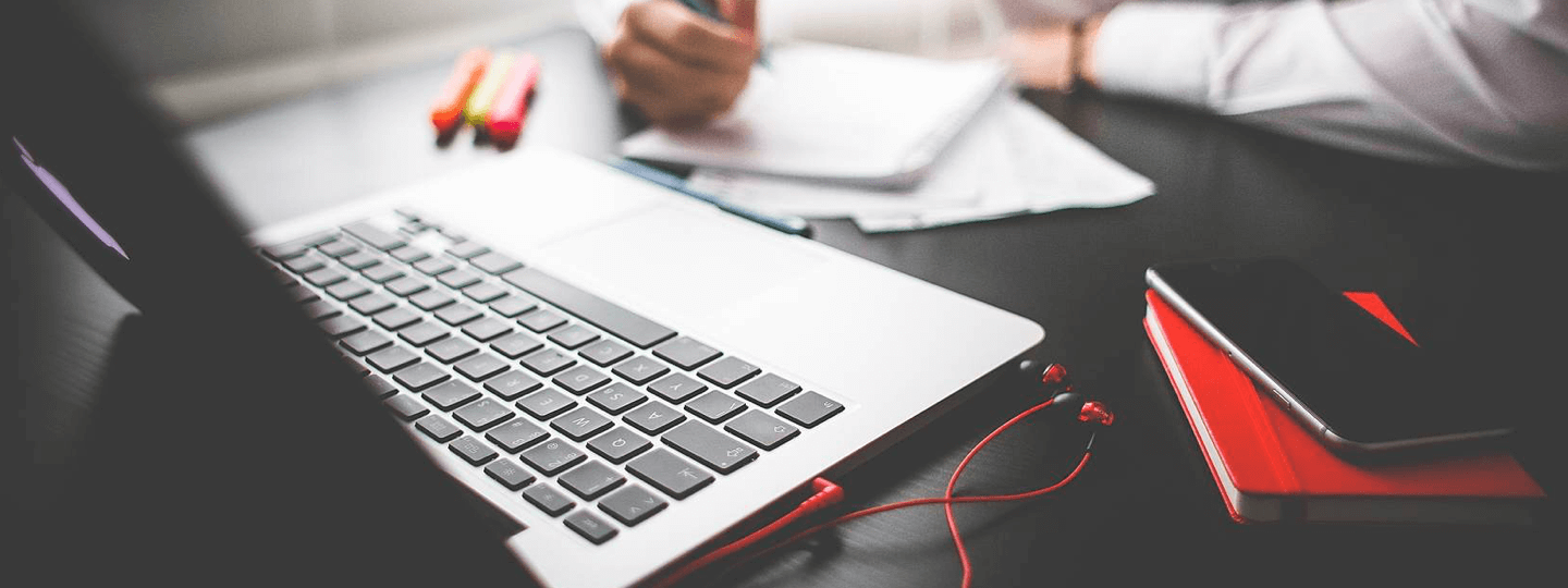 A person writing notes next to a laptop and iPhone