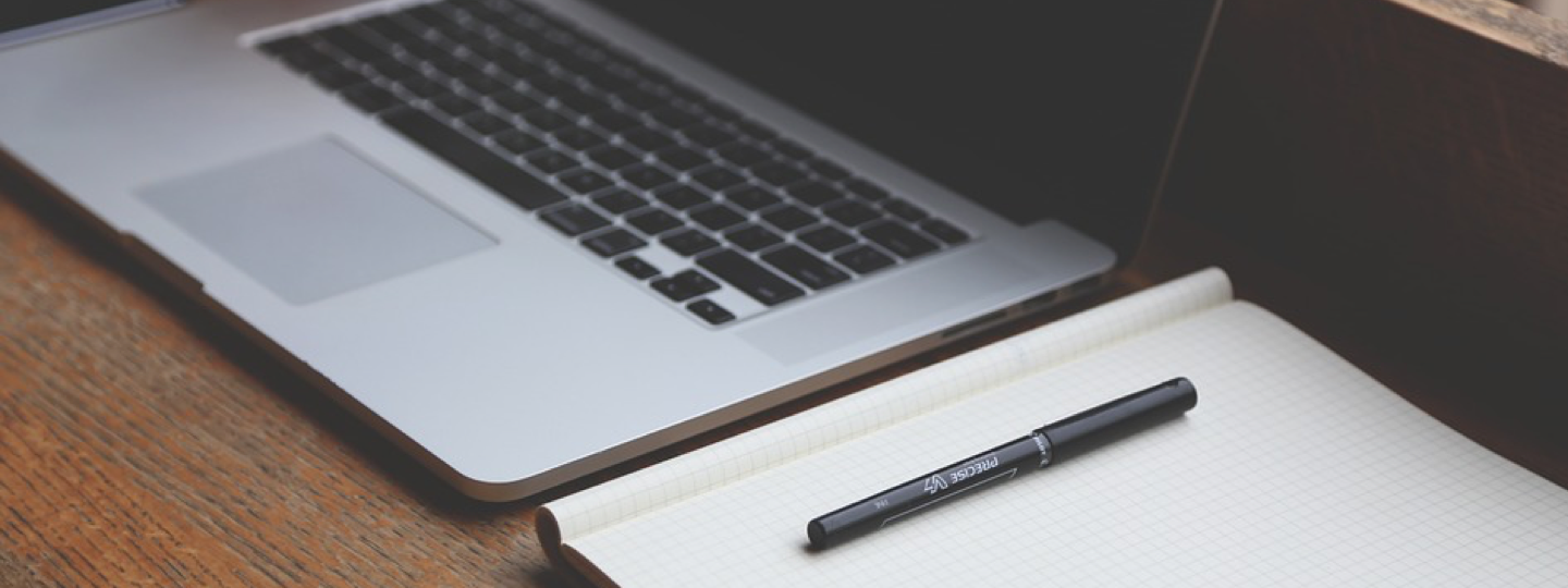 A notepad and pen next to a laptop computer