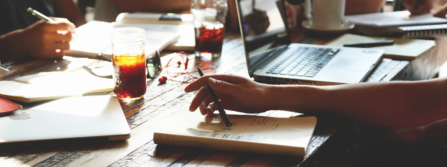 People working at a crowded table with notepads, laptops and drinks