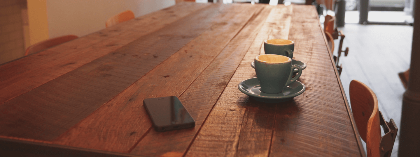 Two coffee cups and an iPhone on a wooden table