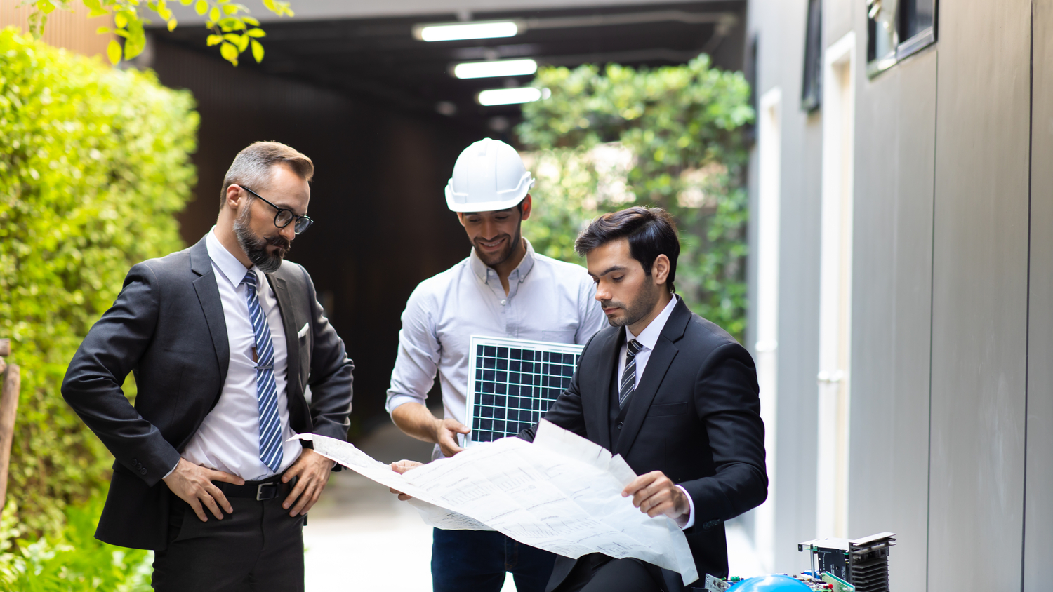 Three men in suits collaborating over design plans.