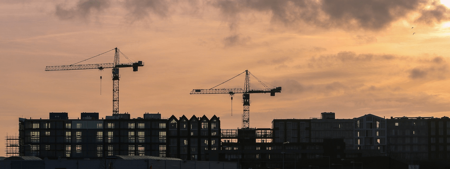 Two cranes sit on top of buildings at sunset