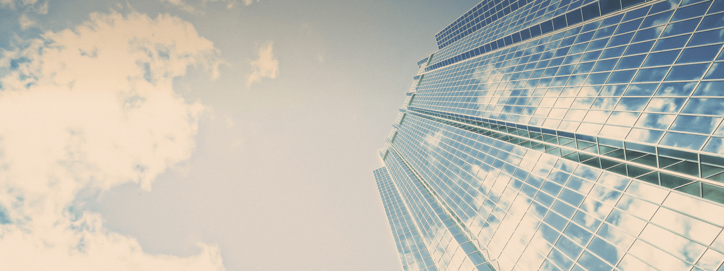 A view looking up a large high rise with a cloudy blue sky