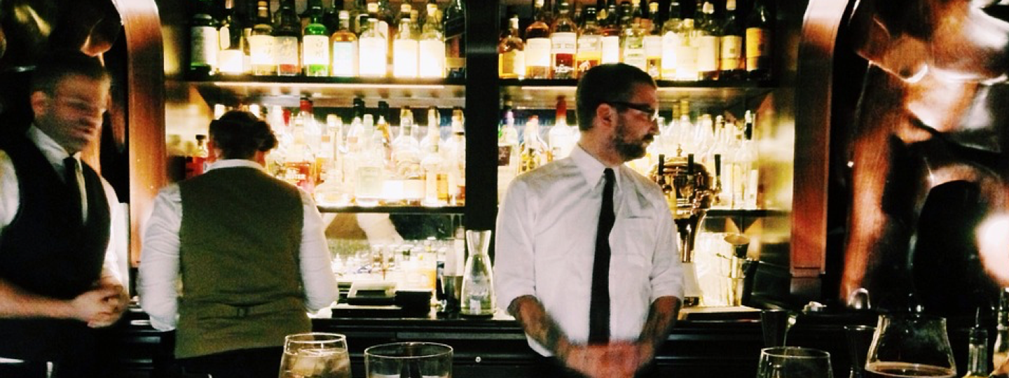 Inside view of an upscale bar with rows of liquor behind a bar tender