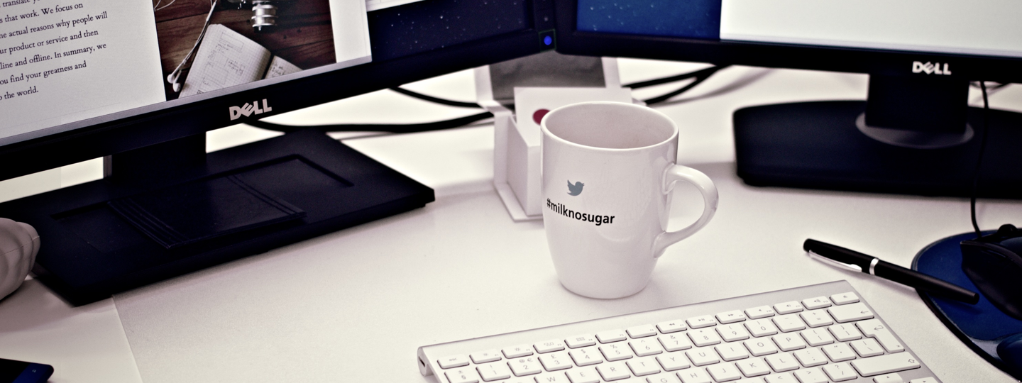 Two Dell monitors, a keyboard and a coffee cup on a desk