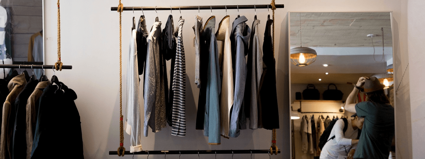 A rack of clothing next to a mirror in an upscale clothing store