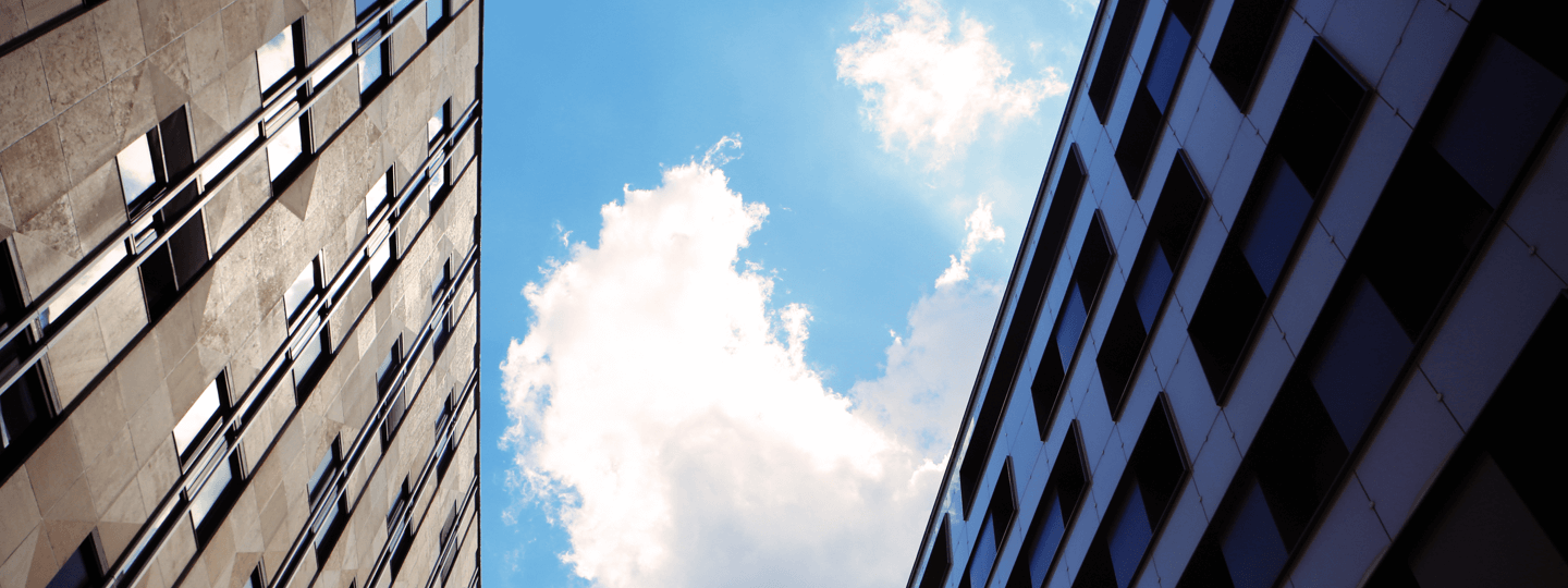 Looking up between two buildings to a partly cloudy sky