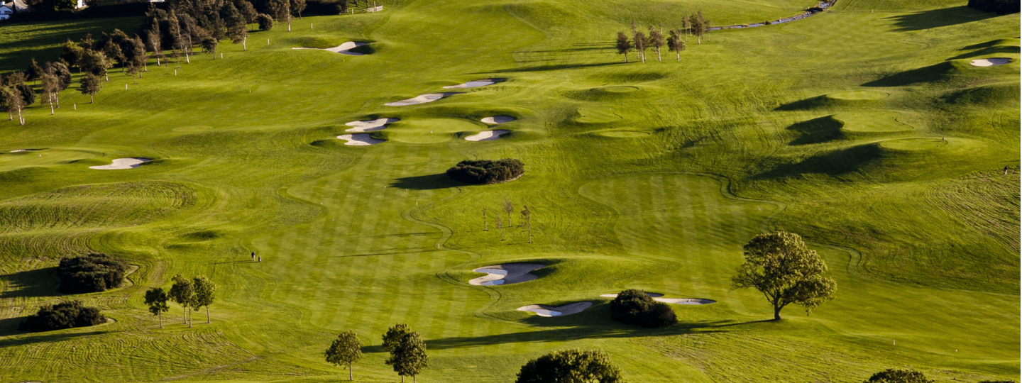 Two people walk through a large, well manicured golf course