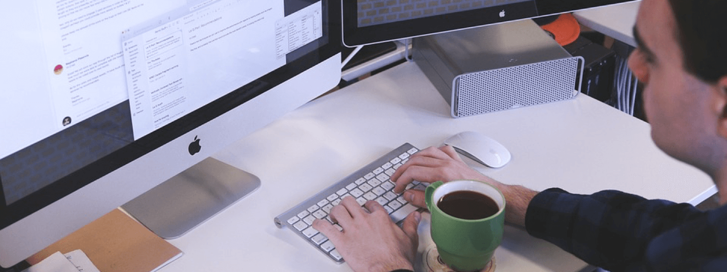 A man with coffee working on a Mac computer