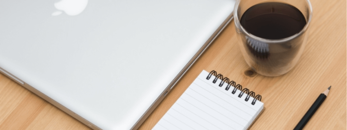 A laptop, a coffee cup and notepad on a table