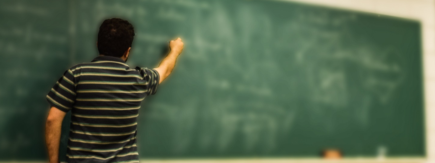 A man in a striped shirt writing on a blurry chalkboard