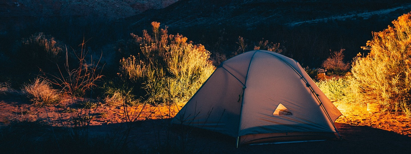 A partially lit up tent amongs sagebrush bushes at dusk