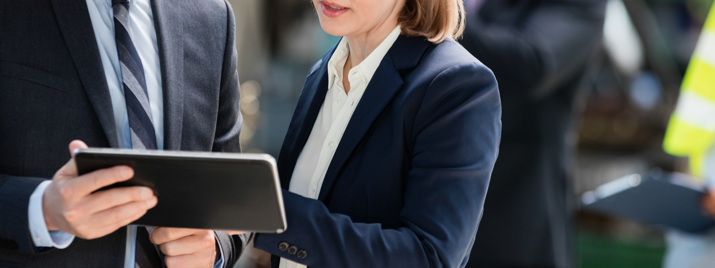 A male and female wearing suits looking at a tablet