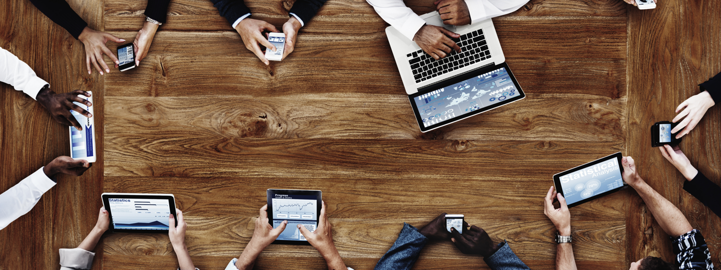 Several professionals sitting around a table with their phones, tablets and laptops