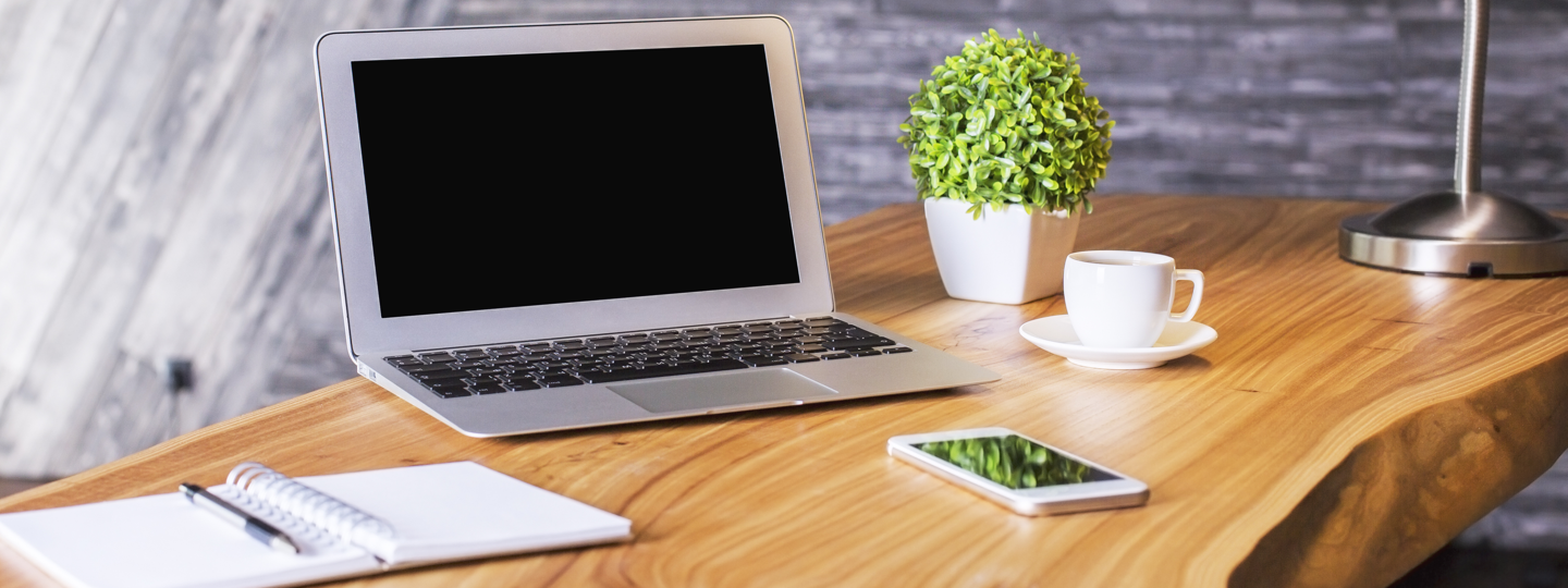 A laptop, notepad and phone sitting on a wood table