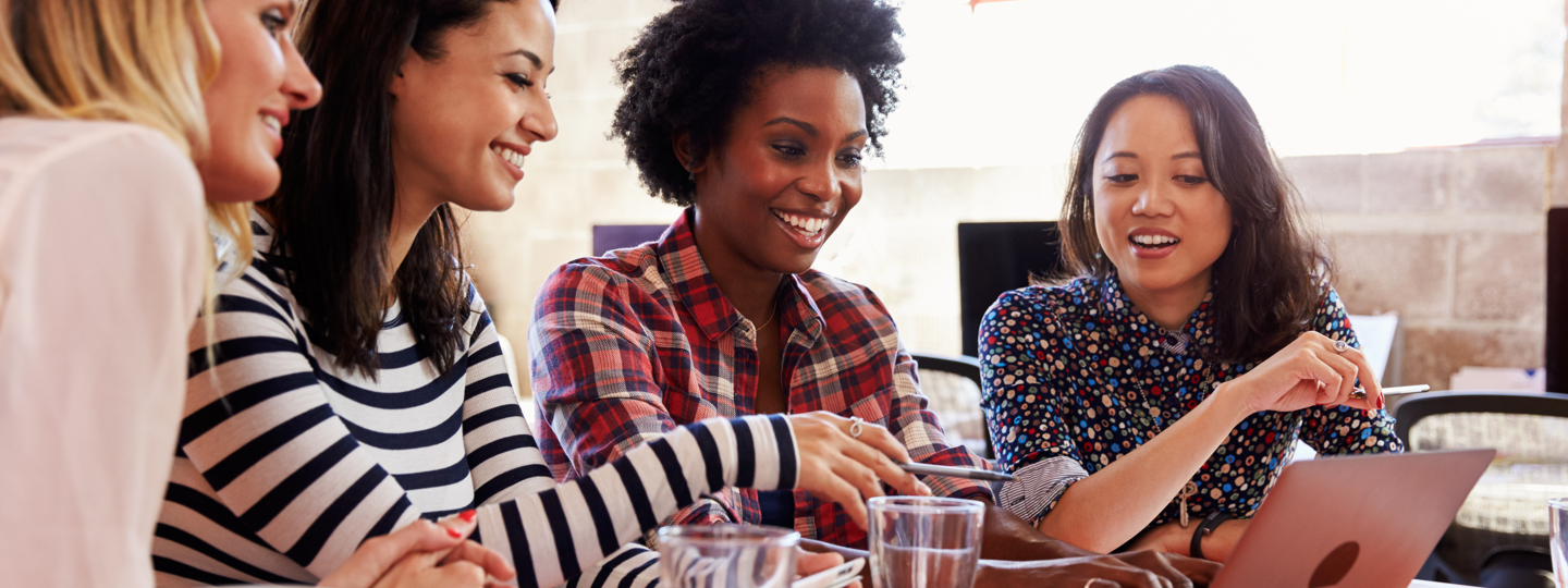 Four young females smiling around a laptop