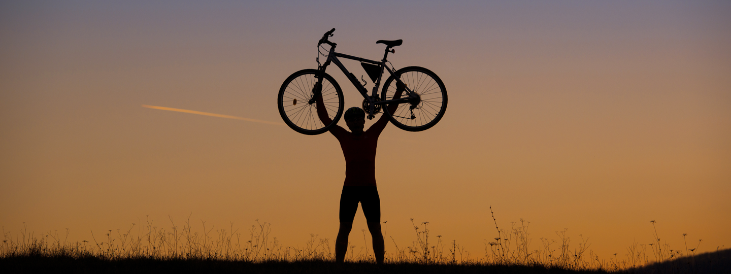 Sillouette of a person holding a bike above their head at sunset