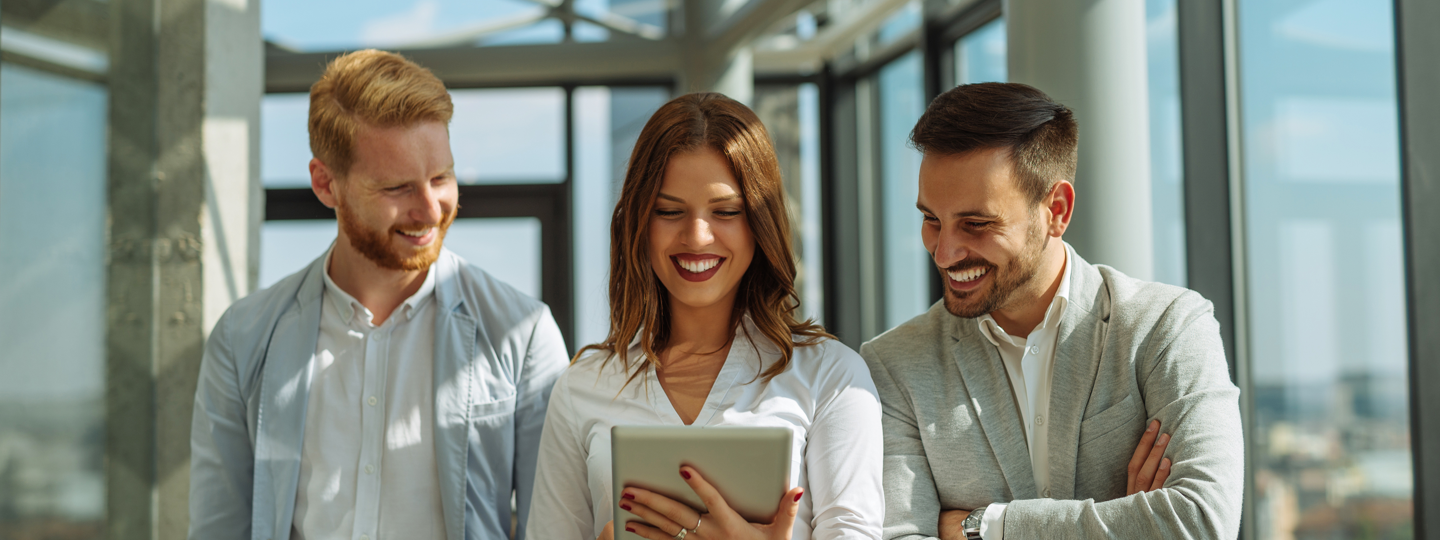 Three people smiling at a tablet inside an office building