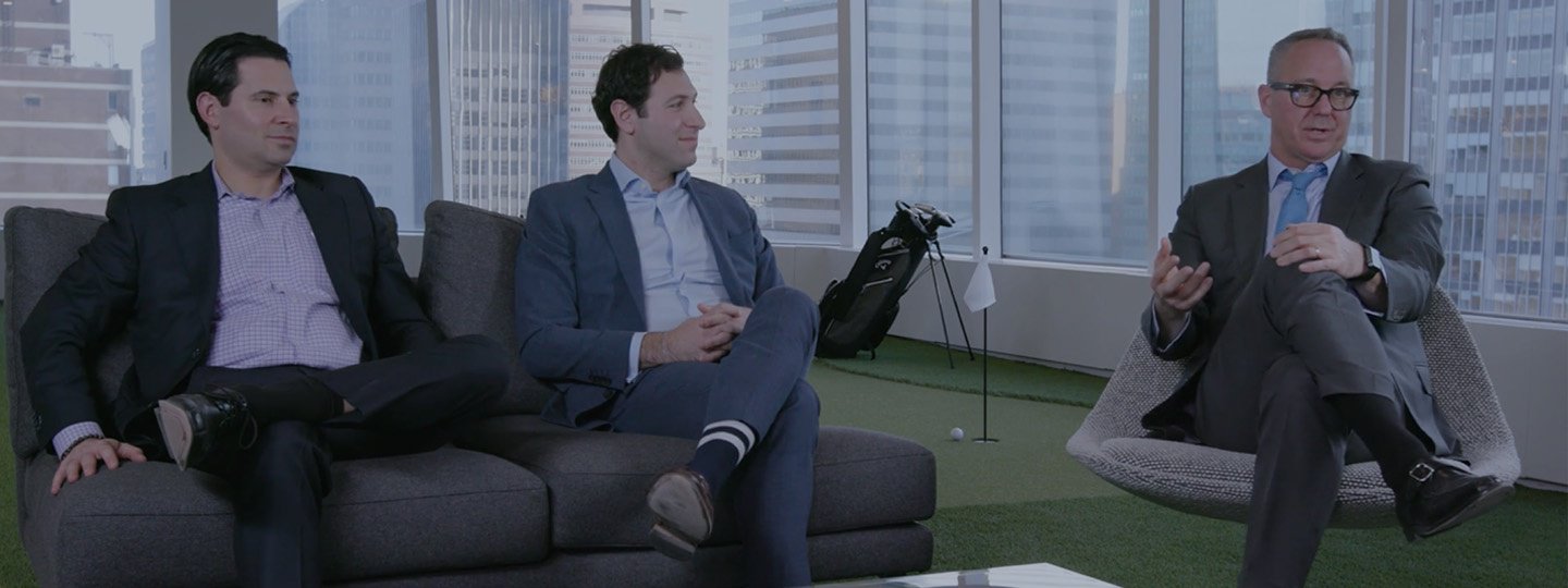 Three men in suits sitting in discussion inside a large office