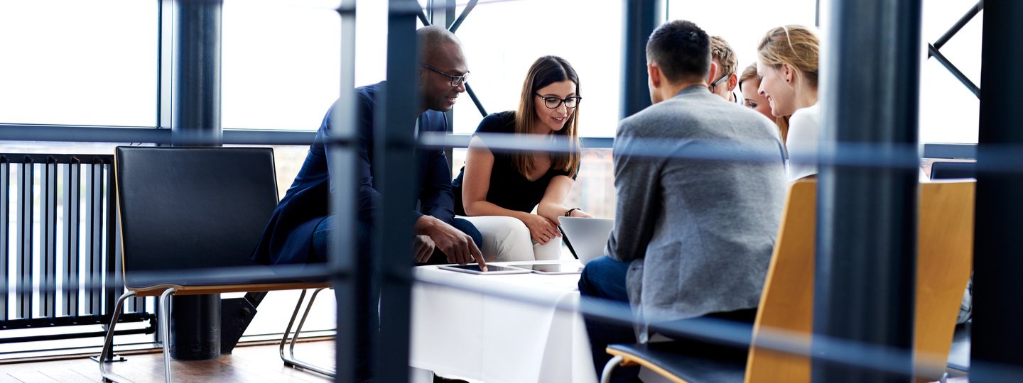 6 professionals collaborating around a laptop in an office