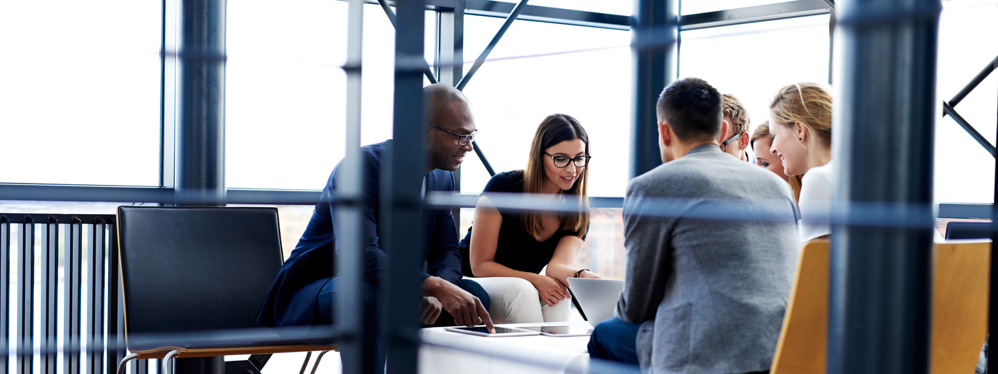 6 professionals collaborating around a laptop in an office