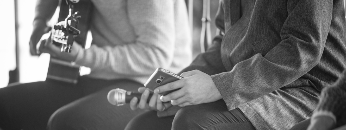 A man playing a guitar next to a man holding a microphone and iPhone