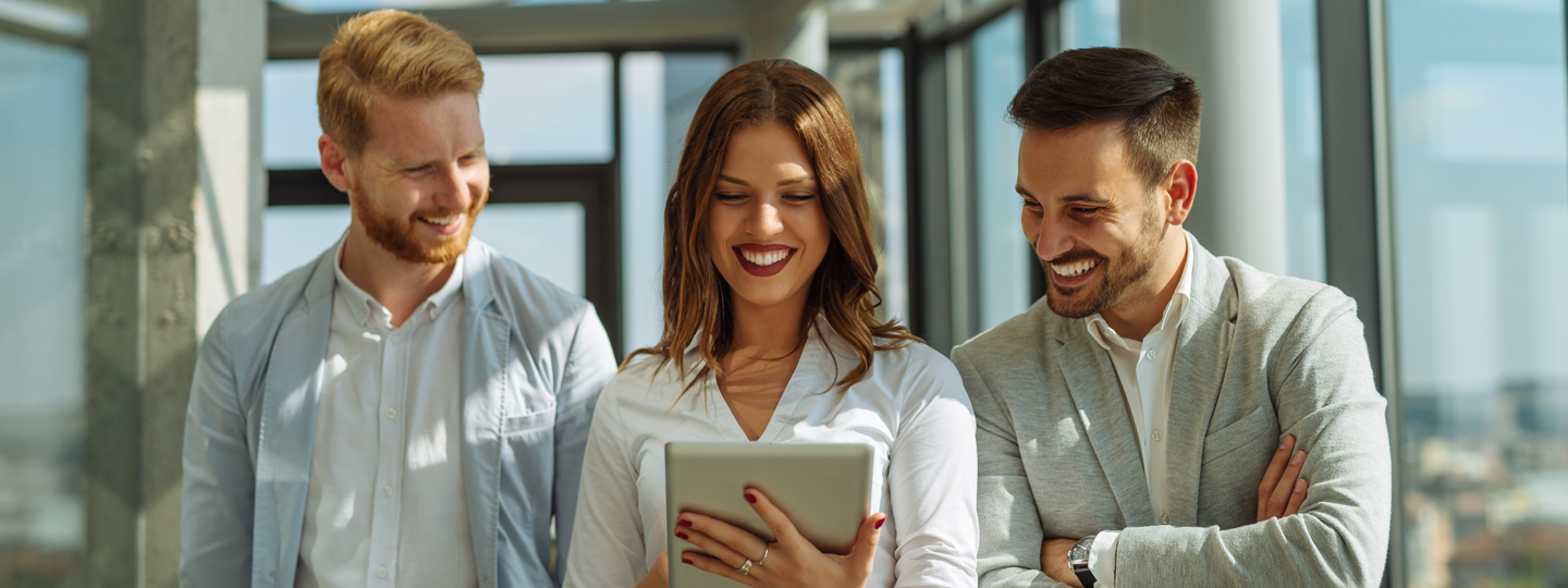 Two men and a women looking at a tablet and smiling