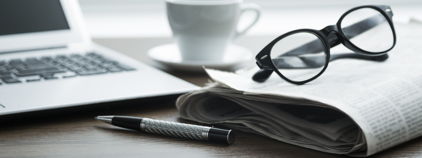 Close up of a laptop, coffee, glasses, paper and a pen