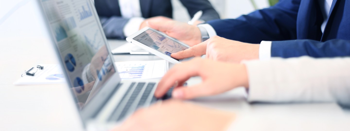 Close up of three men in suits collaborating around computers and tablets