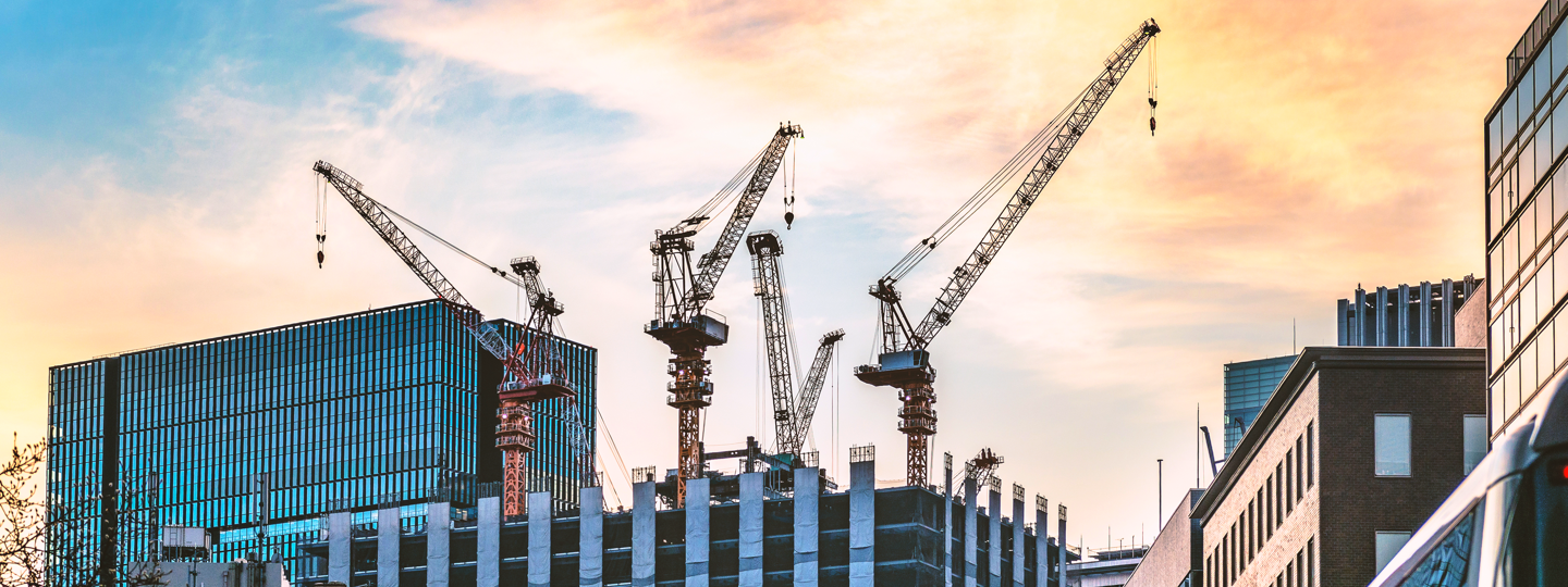 Several cranes on top of an under construction building in a city