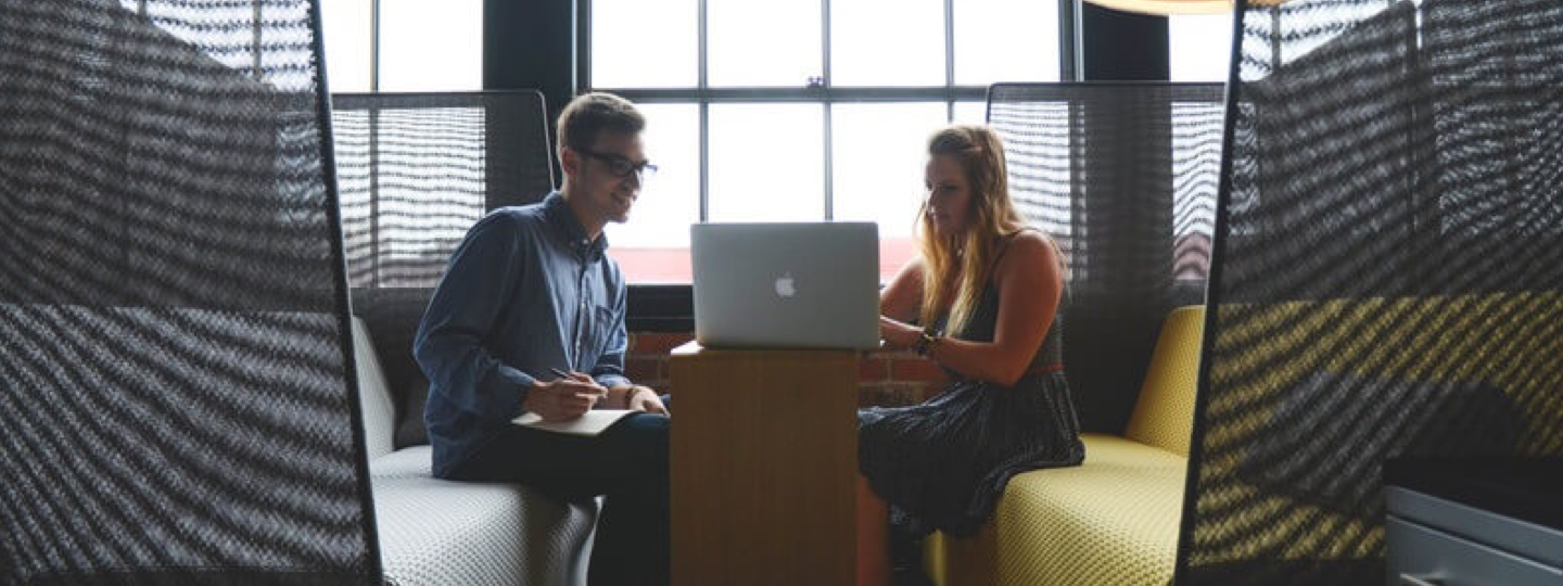 A young male and female sitting on couches collaborating around a laptop