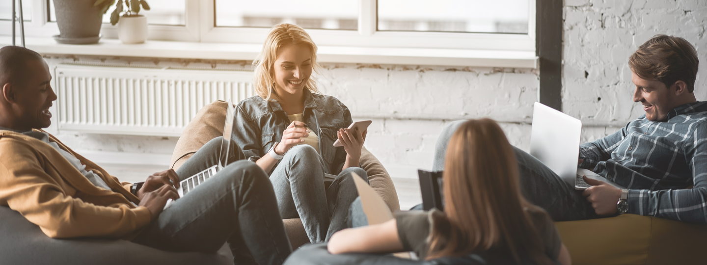 4 young adults sitting on bean bags working on laptops and phones